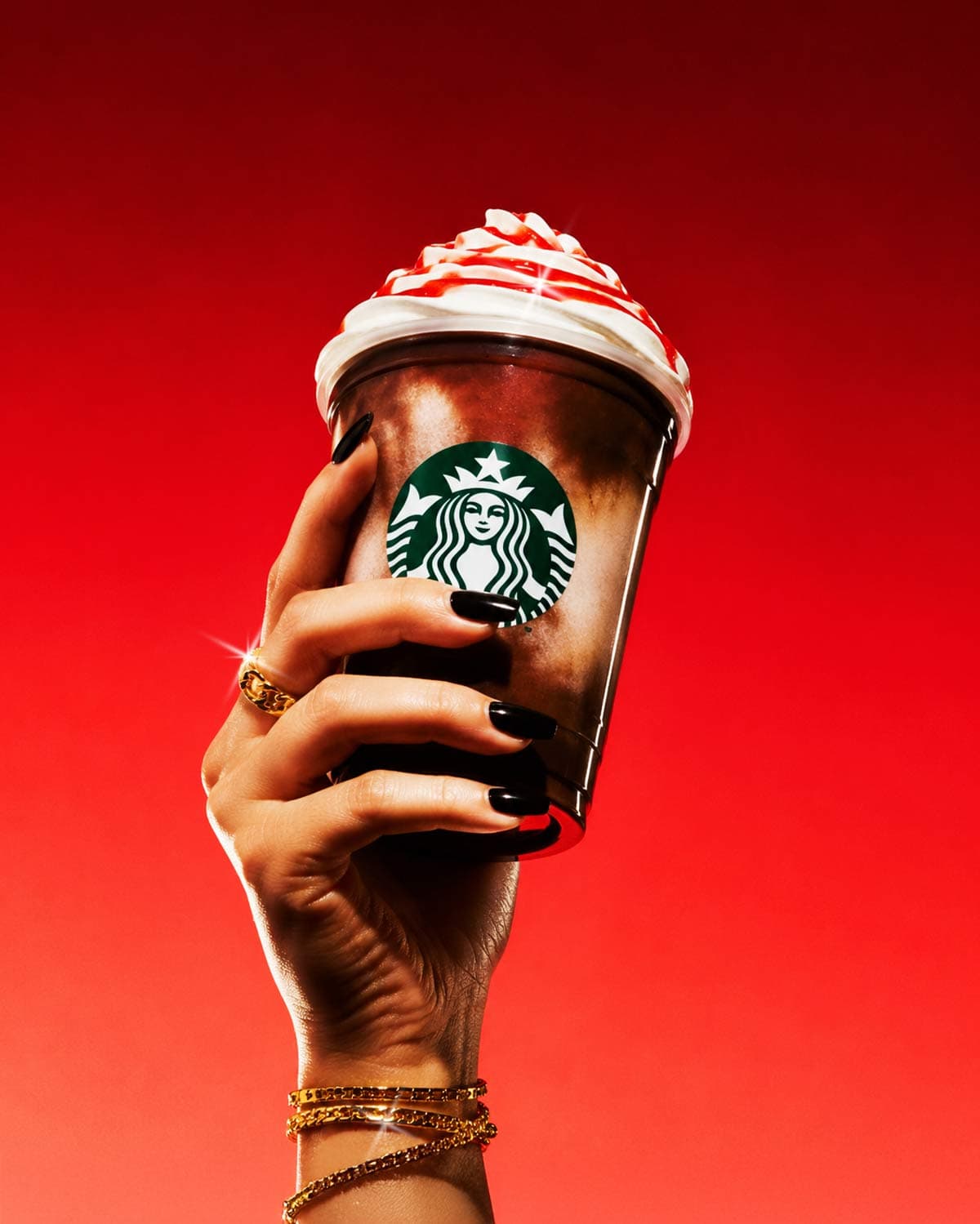 Hand holding themed Frappuccino against crimson background