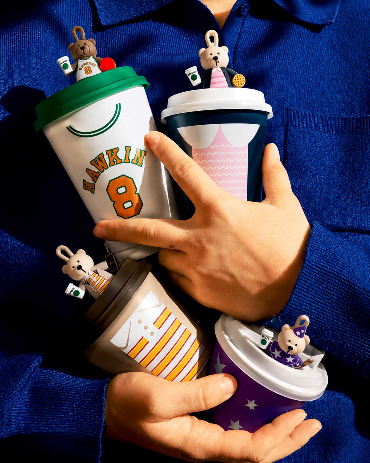 Hands holding trio of themed Starbucks tumblers