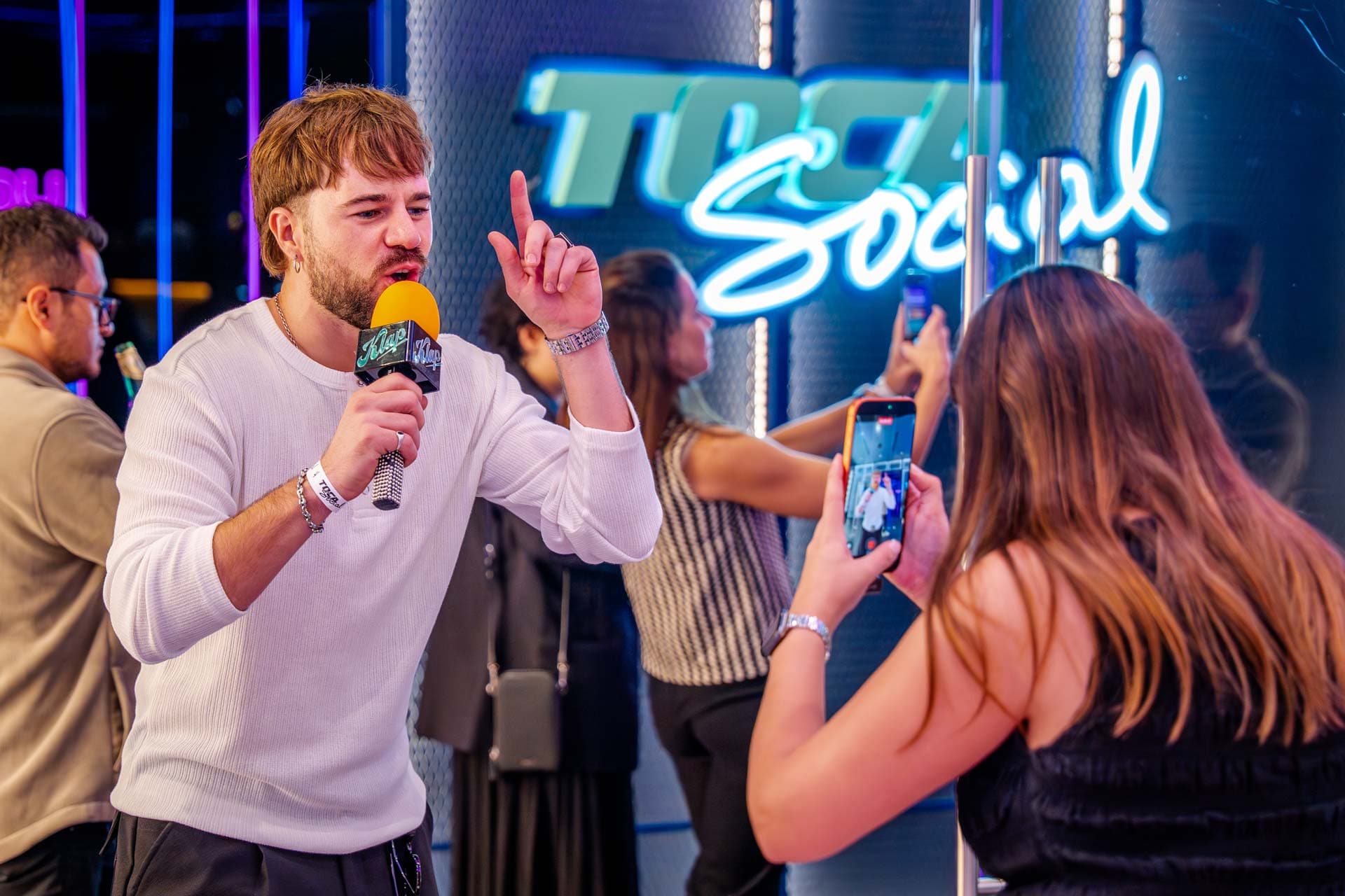 Event host speaking with crowd in front of glowing TOCA Social neon sign