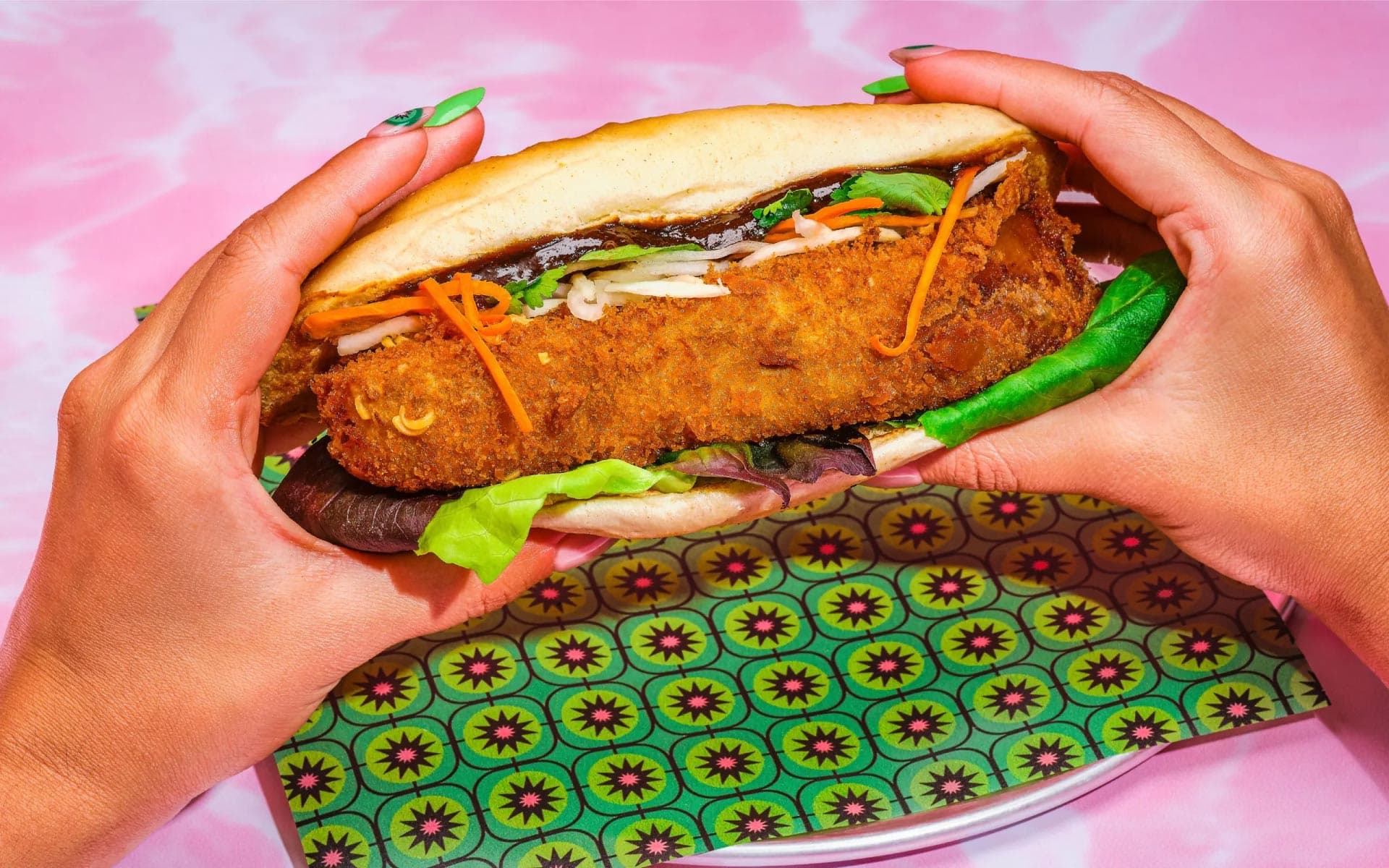 Hands holding crispy Banh Mi sandwich on pink background
